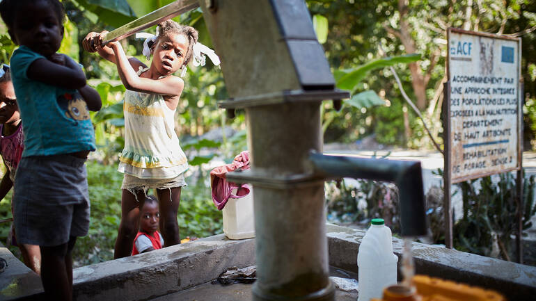 Ein Kind pumpt Wasser aus einem 2008 von Aktion gegen den Hunger errichteten Brunnen, weitere Kinder schauen zu.