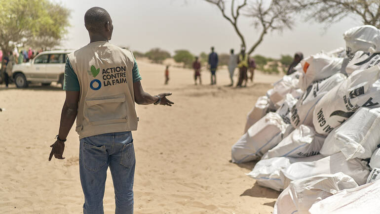 Ein Mitarbeiter von Aktion gegen den Hunger steht neben einer Hilfsgüterlieferung in einem Geflüchtetencamp im Tschad.