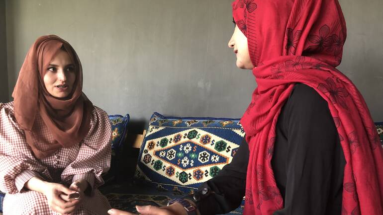 Zwei Beraterinnen aus Afghanistan sprechen auf einem Sofa miteinander über die Gespräche, die sie heute mit Frauen aus Afghanistan über die Hotline für psychosoziale Hilfe geführt haben.