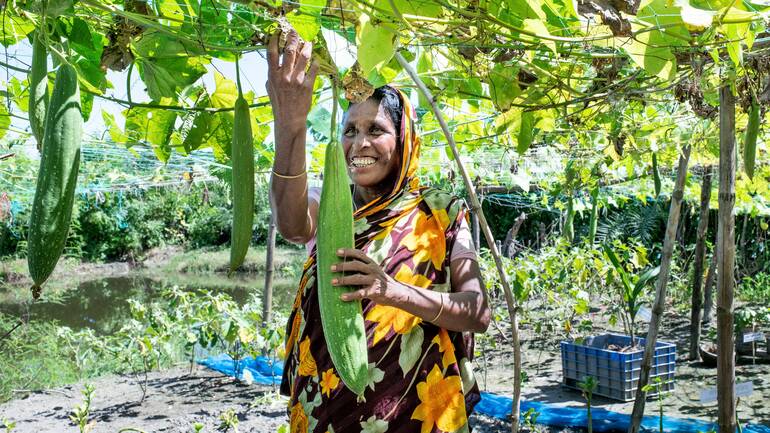 Eine Frau aus Bangladesch pflückt glücklich eine ihrer selbst angebauten Gurken.