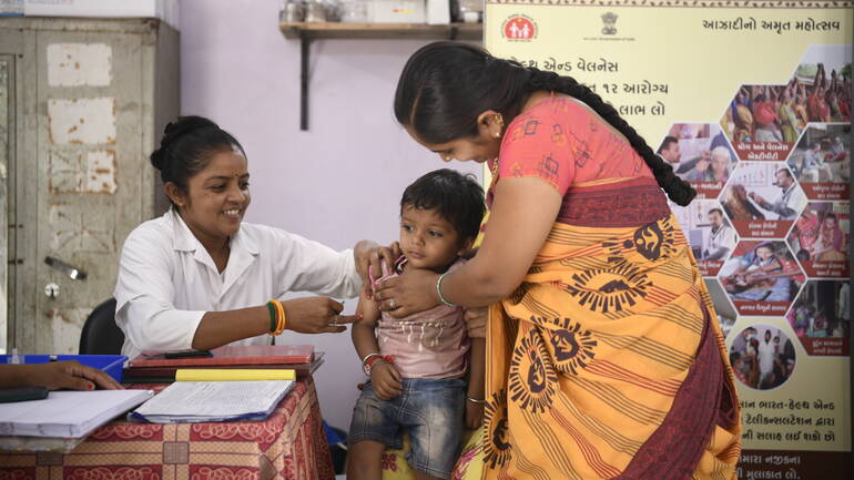 Afsana aus Indien gibt einem kleinen Kind eine Schutzimpfung, das in den Armen seiner Mutter ist. 