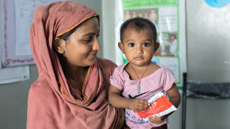Asha aus Pakistan mit ihrer 15 Monate alten Tochter Ishani, die Erdnusspaste in der Hand hat. 