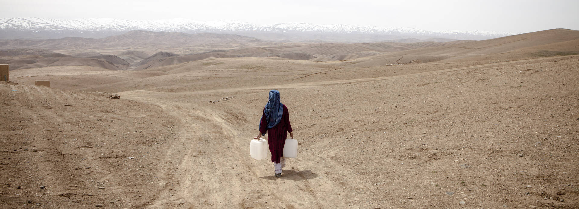 Eine Frau trägt Wasserkanister durch die weite, karge Landschaft Zentralafghanistans