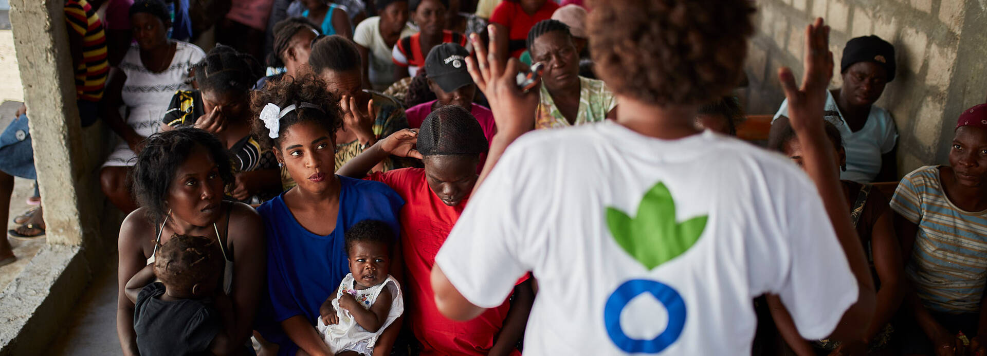 Eine Mitarbeiterin von Aktion gegen den Hunger erklärt einer Gruppe Frauen, Männer und Kinder aus Haiti, wie sie sich mit gesunder Ernährung und Hygiene vor Cholera schützen können.