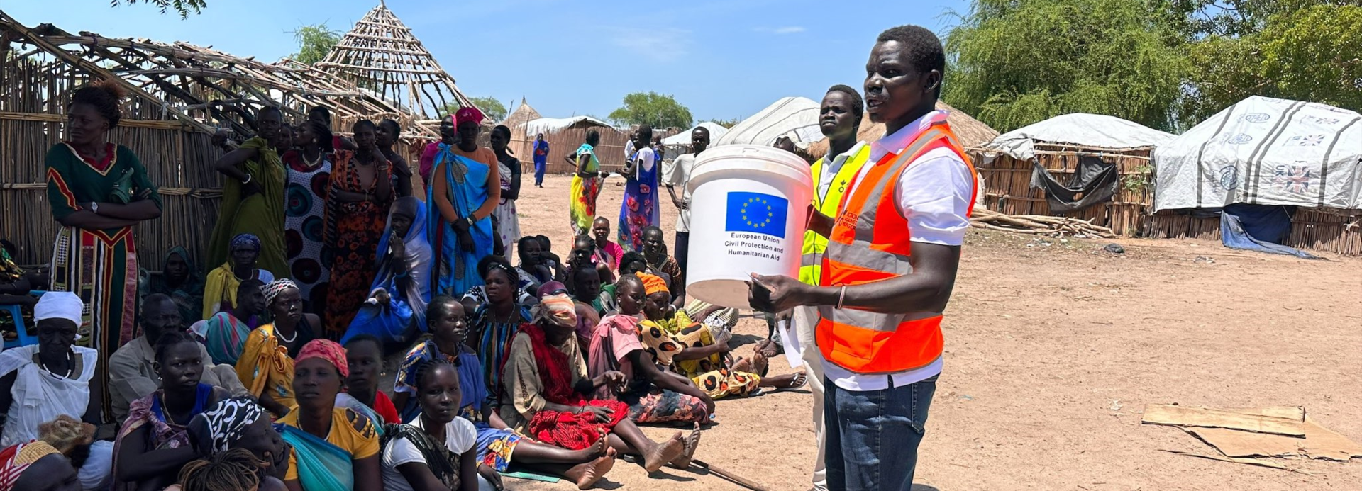 Ein Mitarbeiter von Aktion gegen den Hunger spricht zu Frauen, die im Schatten vor ihm sitzen und aus dem Sudan zurück in den Südsudan geflohen sind.