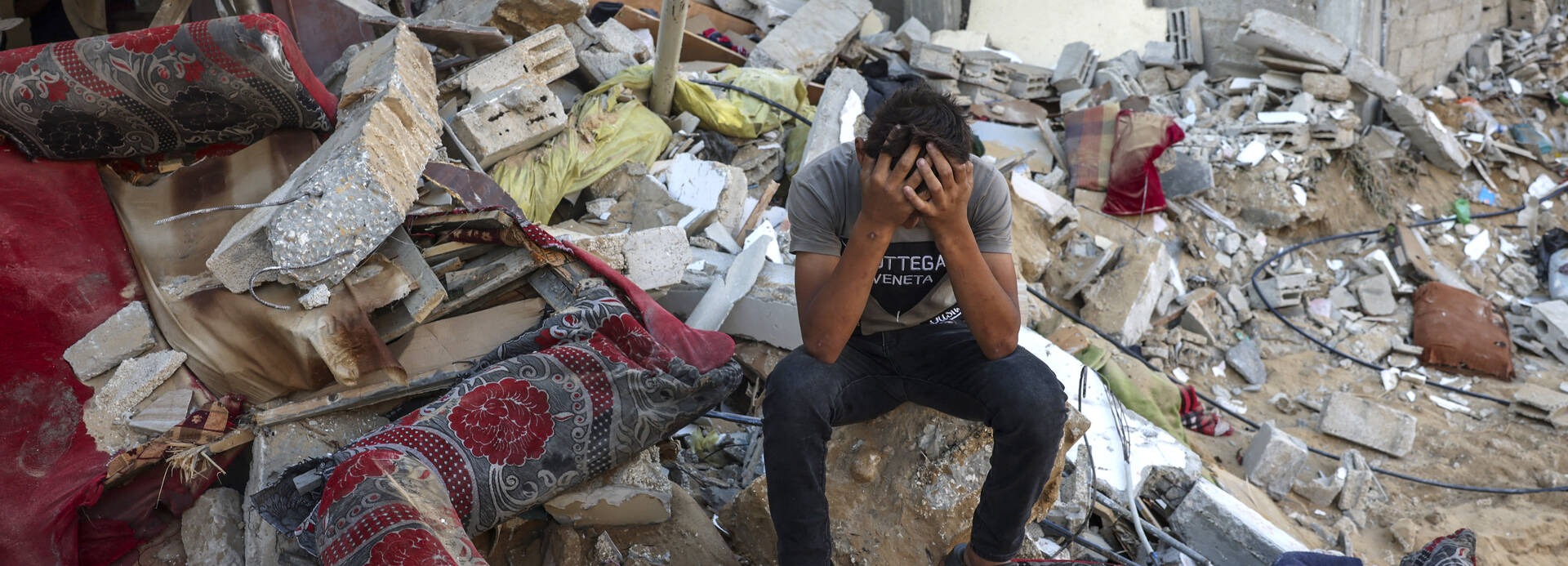 Ein palästinensischer Jugendlicher sitzt auf den Überresten seines zerstörten Hauses und vergräbt den Kopf in den Händen.