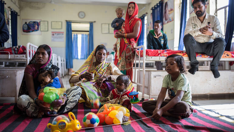 Familien sitzen und stehen rund um Spielzeug in der Klinik in Indien.