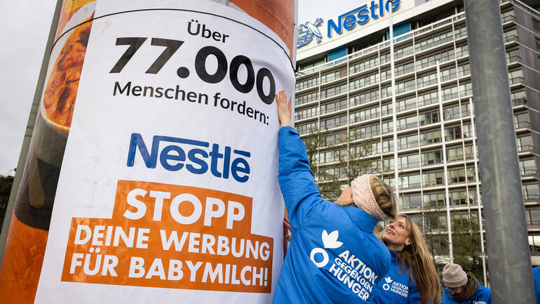 Mitarbeiterinnen von Aktion gegen den Hunger befestigen ein Plakat zum Erfolg der Petition vor der Nestlé-Zentrale in Frankfurt am Main.