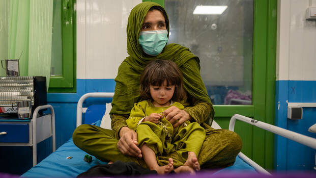 Eine afghanische Mutter sitzt zusammen mit ihrer Tochter auf einem Bett in unserer Ernährungsstation in einer Klinik in Kabul.