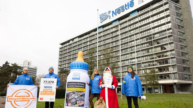 Das Team von Aktion gegen den Hunger und der Nikolaus stehen zusammen mit einer aufblasbaren Babymilchflasche vor der Nestlé-Zentrale in Frankfurt am Main.