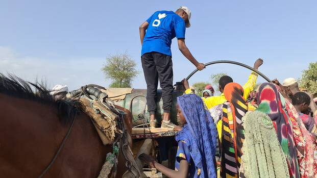 Ein Mitarbeiter von Aktion gegen den Hunger beim Verteilen von sauberem Wasser an geflüchtete Menschen aus dem Sudan im Tschad.