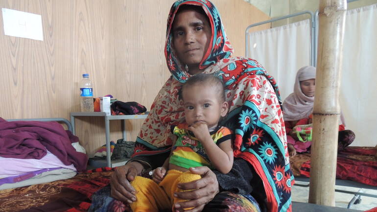 Die einjährige Nila im Schoß ihrer Mutter auf dem Bett einer Krankenstation in Bangladesch