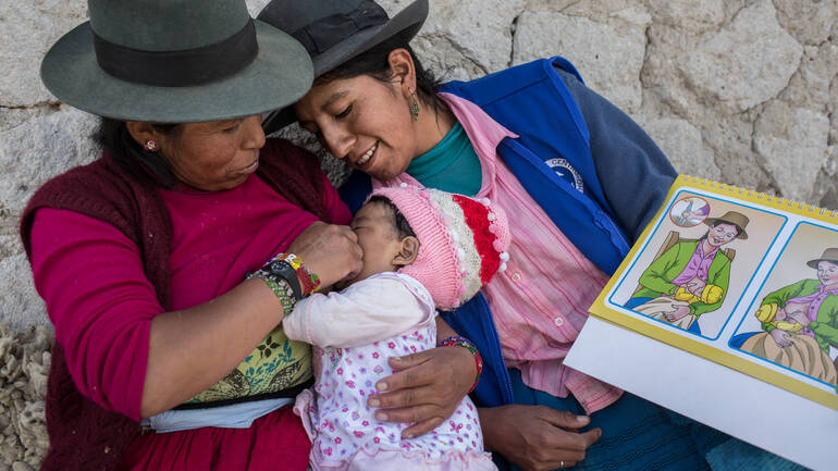 Stillberaterinnen in Peru unterstützen Mütter dabei, das Stillen zu lernen. Zwei Frauen aus Peru stillen ein kleines Mädchen nach einer bildlichen Anleitung.