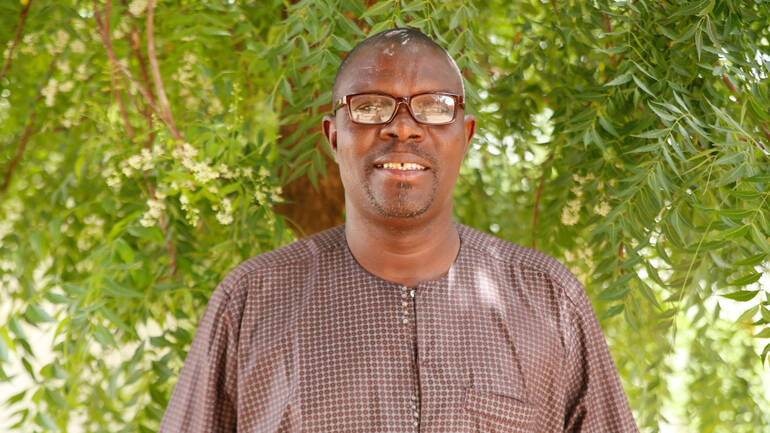 Mama Fall steht vor einem Baum in seiner Heimat im Senegal Mama Fall steht vor einem Baum in seiner Heimat im Senegal