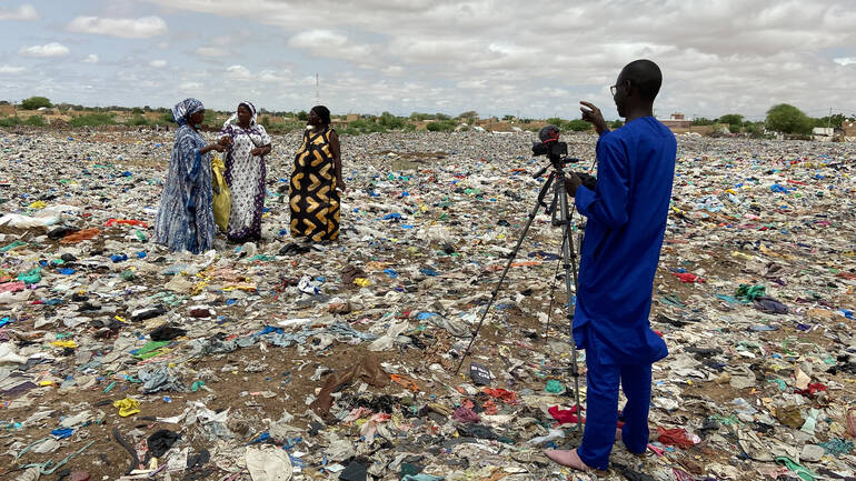 Ein Fotograf weist drei Frauen an, sie stehen auf einem Müllfeld im Senegal