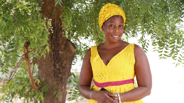Aissatou Waba Nballo steht in gelb gekleidet vor einem Baum in ihrem Dorf im Senegal