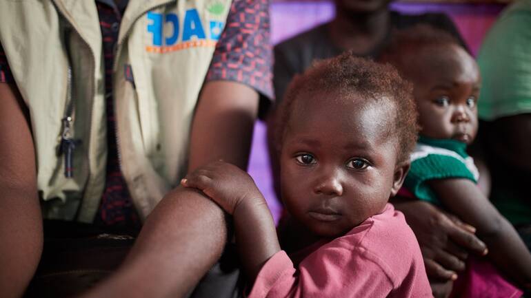 Kind hält den Arm eines Helfers von Aktion gegen den Hunger Kind hält den Arm eines Helfers von Aktion gegen den Hunger