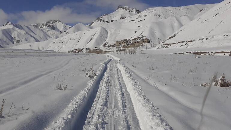 Ein freigeschaufelter Weg durch den Schnee, im Hintergrund ein Dorf in Afghanistan.