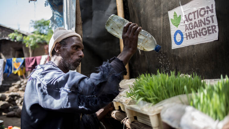 Ein Mann aus Äthiopien gießt keimende Pflanzen mithilfe einer zur Gießkanne umfunktionierten Wasserflasche