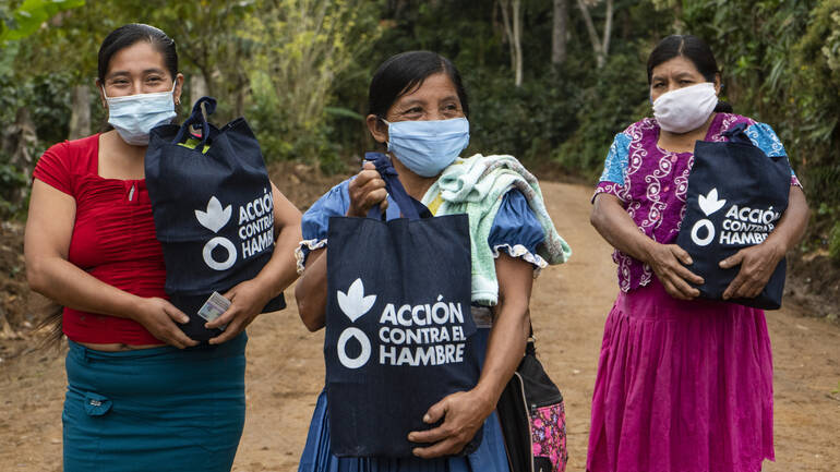 Drei Frauen aus Guatemala tragen Gesichtsmasken und freuen sich über Hygienekits in Tüten von Aktion gegen den Hunger