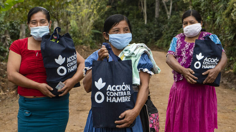 In Guatemala leiden die Menschen unter den Auswirkungen der Coronavirus-Pandemie – Aktion gegen den Hunger hilft. Drei Frauen aus Guatemala tragen Gesichtsmasken und freuen sich über Hygienekits in Tüten von Aktion gegen den Hunger