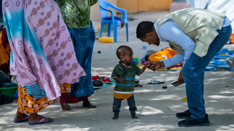 Ein Mitarbeiter hält die Hand eines kleinen Jungen im Hof eines Krankenhauses in Somalia, daneben zwei Frauen