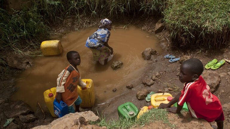 Kinder füllen Wasserkanister an einem kleinen, schmutzigen Wasserloch auf Drei Kinder füllen Wasserkanister an einem sehr kleinen, verschmutzten Wasserloch auf.