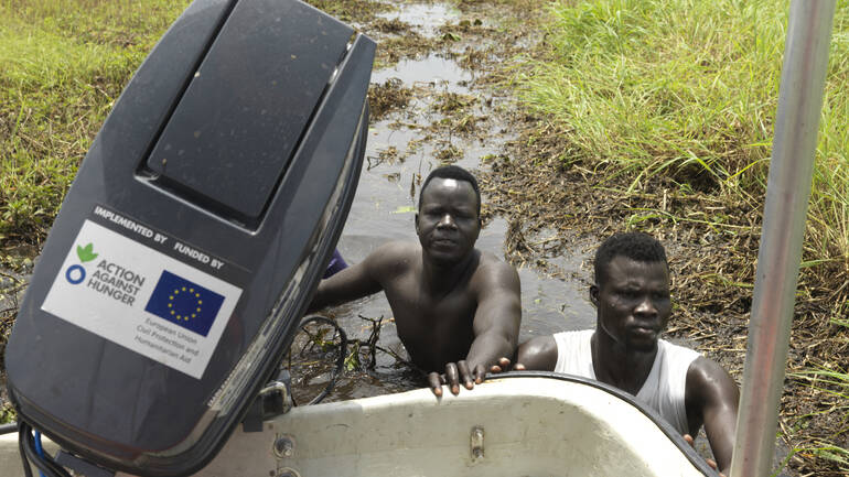 Zwei Männer schieben ein Boot von Aktion gegen den Hunger durch die Sümpfe - die Wasserstraße ist noch nicht gebaut Zwei Männer schieben ein Boot von Aktion gegen den Hunger durch die Sümpfe - die Wasserstraße ist noch nicht gebaut