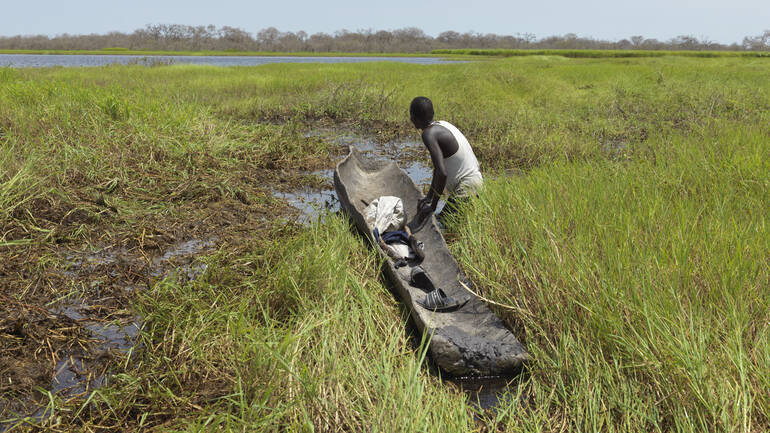 Ein Mann aus dem Südsudan versucht sein altes Baumstamm-Kanu durch ein überflutetes Feld zu ziehen