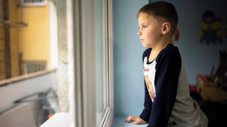 Ein aus der Ukraine geflüchteter Junge schaut vor der Musiktherapie-Stunde voller Gedanken aus dem Fenster.
