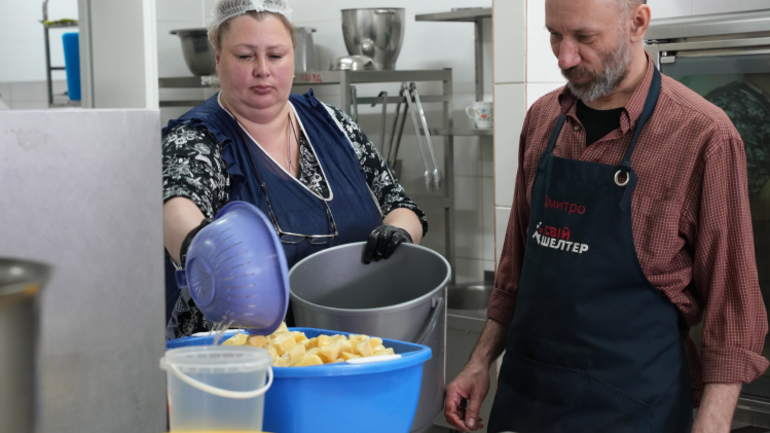 Zwei Küchenhelfer*innen bereiten Kartoffeln in einer großen Küche vor – für warme Mahlzeiten. Zwei Küchenhelfer*innen bereiten Kartoffeln in einer großen Küche vor – für warme Mahlzeiten.