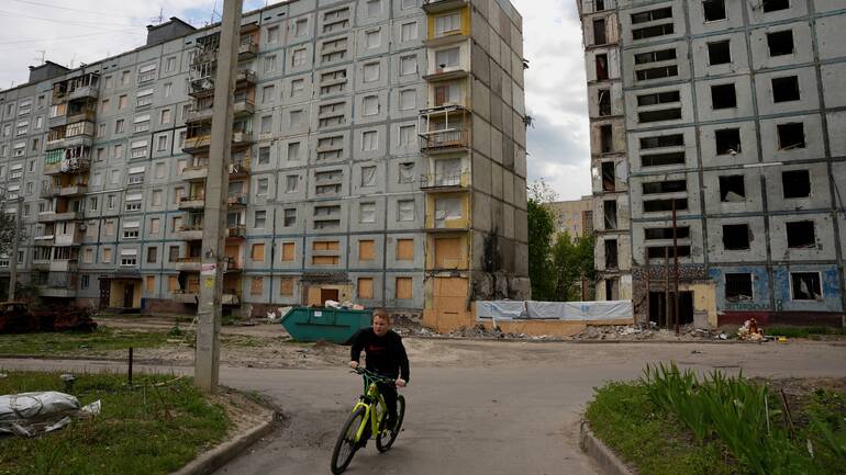 Ein Junge fährt auf dem Fahrrad vor von Bomben zerstörten Wohnblöcken in der Ukraine entlang.