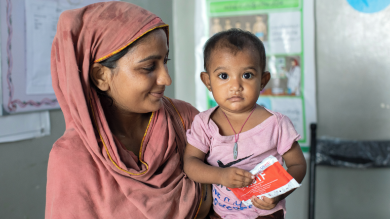 Asha aus Pakistan mit ihrer 15 Monate alten Tochter Ishani, die Erdnusspaste in der Hand hat. Asha aus Pakistan mit ihrer 15 Monate alten Tochter Ishani, die Erdnusspaste in der Hand hat.