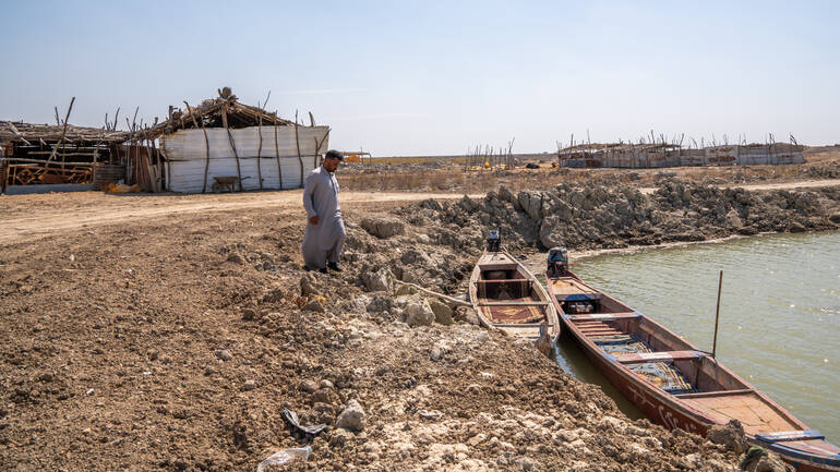 Ein Mann im Irak läuft über die ausgetrocknete Erde zu seinem Ruderboot in einem kleinen See. Ein Mann im Irak läuft über die ausgetrocknete Erde zu seinem Ruderboot in einem kleinen See.