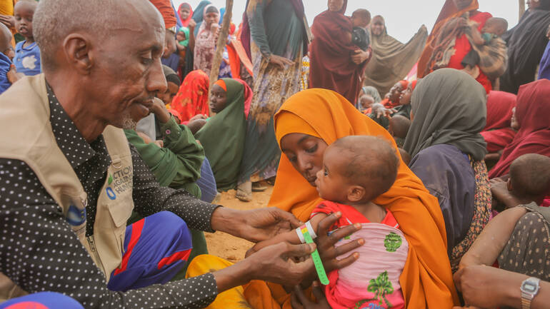Unsere Teams untersuchen weltweit in Krisen- und Konfliktgebieten Kinder auf Mangelernährung. Im Geflüchtetencamp in Hudur, Somalia, untersucht unser mobiles Gesundheitspersonal die elf Monate alte Awliyo Ali mit einem MUAC-Band auf Mangelernärhung, während ihre Mutter Hawa Muse ihre Hand hält.