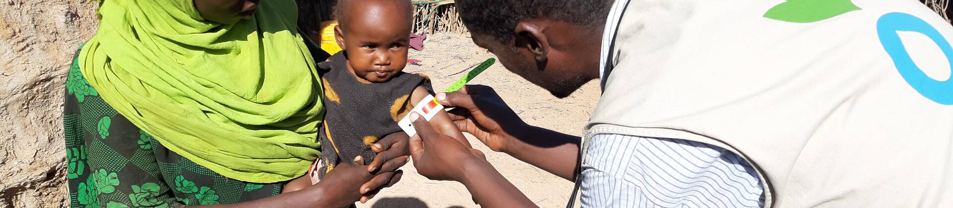 Ein Mitarbeiter von Aktion gegen den Hunger untersucht ein Kleinkind in den Armen der Mutter auf Mangelernährung.