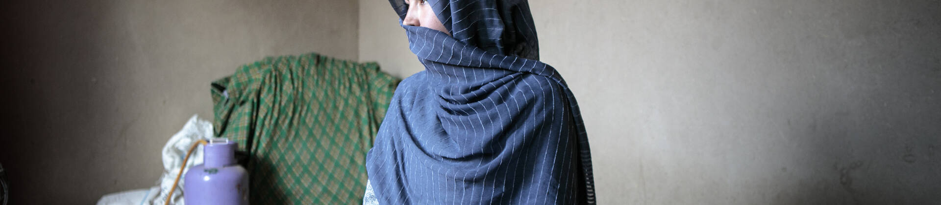 Frauen dürfen ihre Stimme in Afghanistan kaum noch erheben. Eine Frau aus Afghanistan sitzt in ihrem Zuhause und schaut zur Seite. Ein blaues Tuch bedeckt ihren Kopf und ihren Mund.