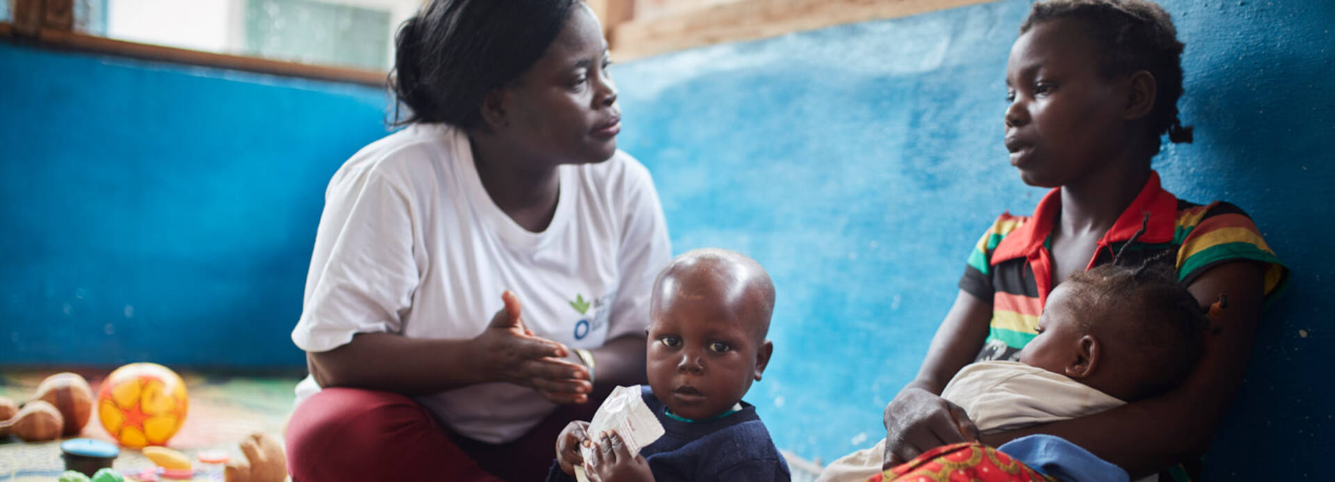 Helferin von Aktion gegen den Hunger hört Mutter mit ihren Kindern zu.