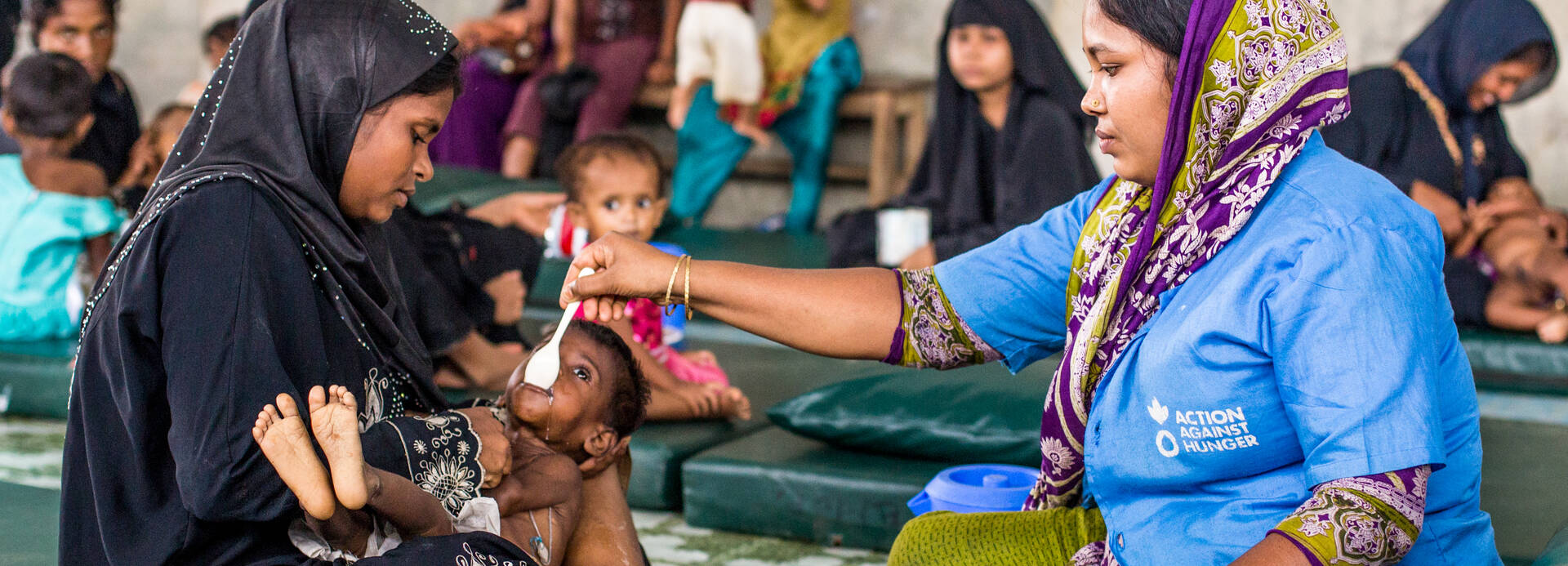 Mitarbeiterin von Aktion gegen den Hunger füttert Kind in Bangladesch.