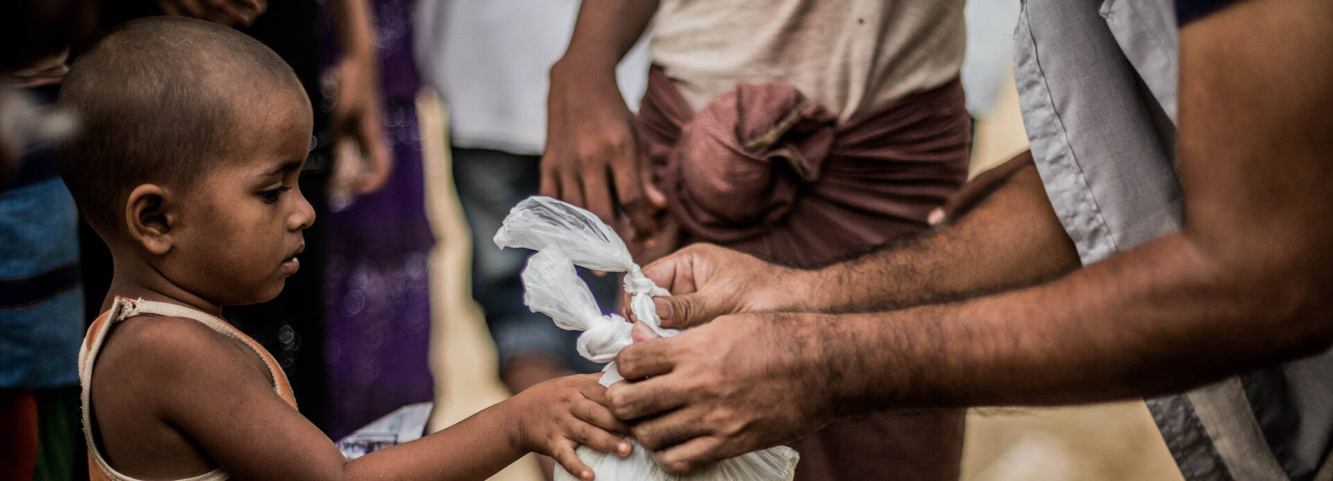 Ein kleiner Rohingya-Junge erhält einen Beutel mit Nahrung.