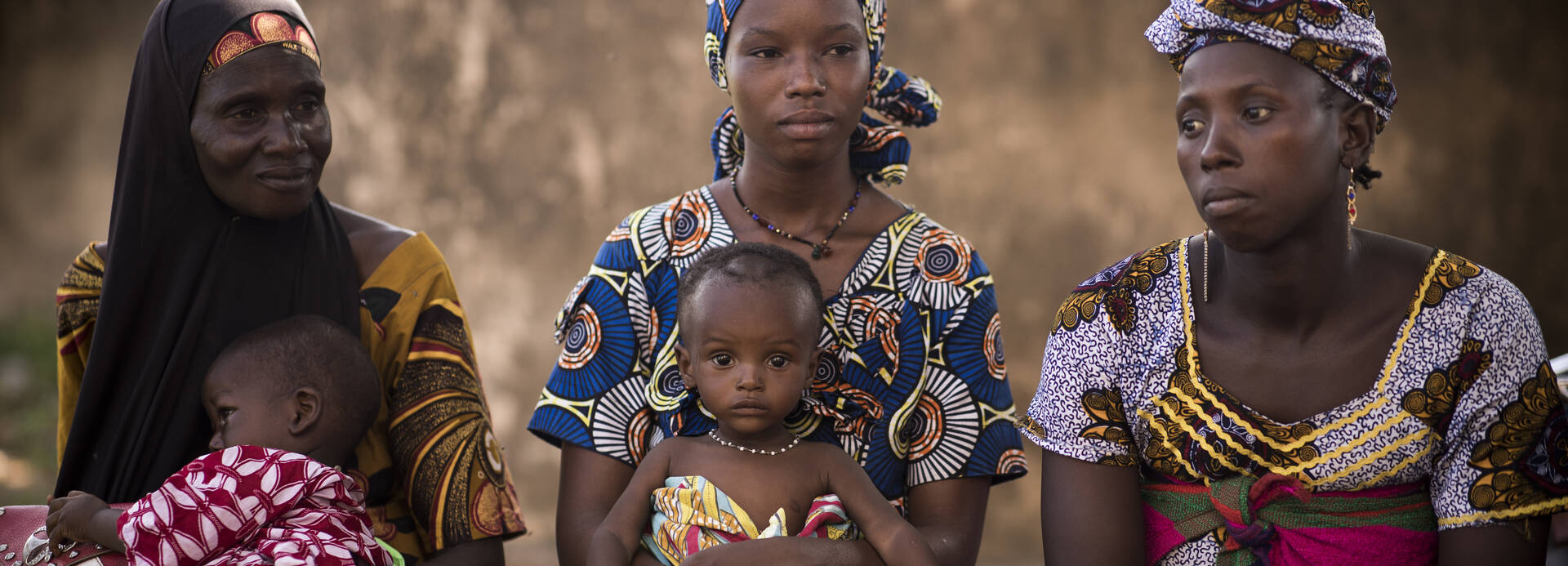Frauen in Mali sitzen zusammen mit ihren Kindern auf dem Schoß.