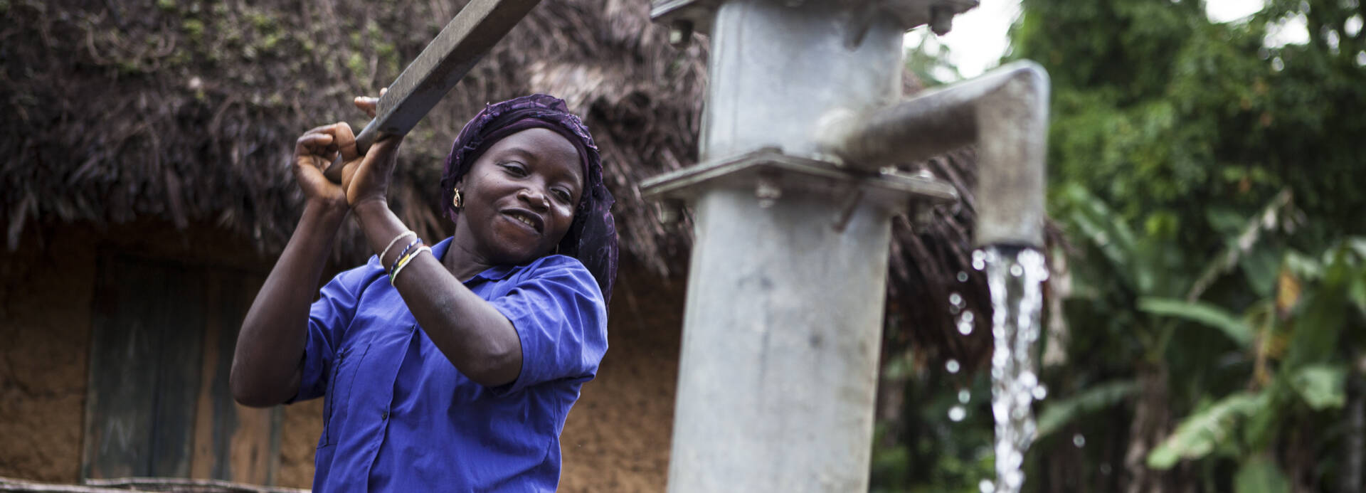 Frau in Sierra Leone betätigt Wasserpumpe.