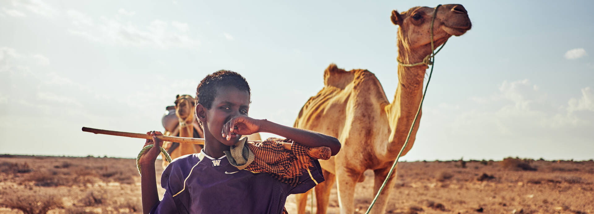 Junge in Somalia steht mit seinem Kamel in der Wüste.