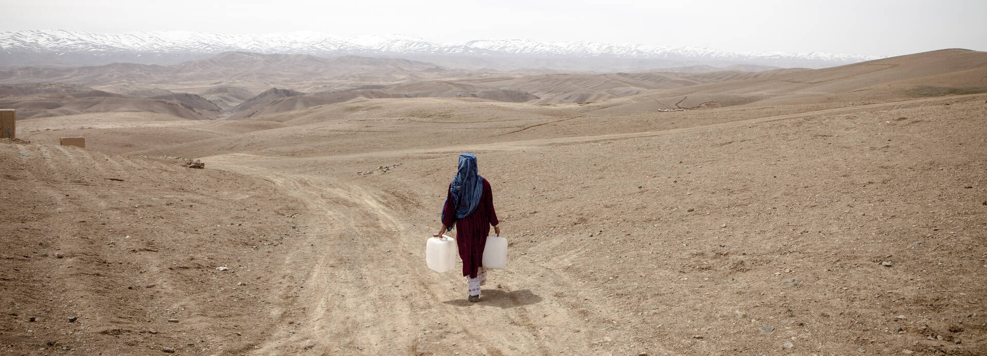 Eine Frau trägt 2 Wasserkanister durch die weite, karge Landschaft Zentralafghanistans Eine Frau trägt Wasserkanister durch die weite, karge Landschaft Zentralafghanistans