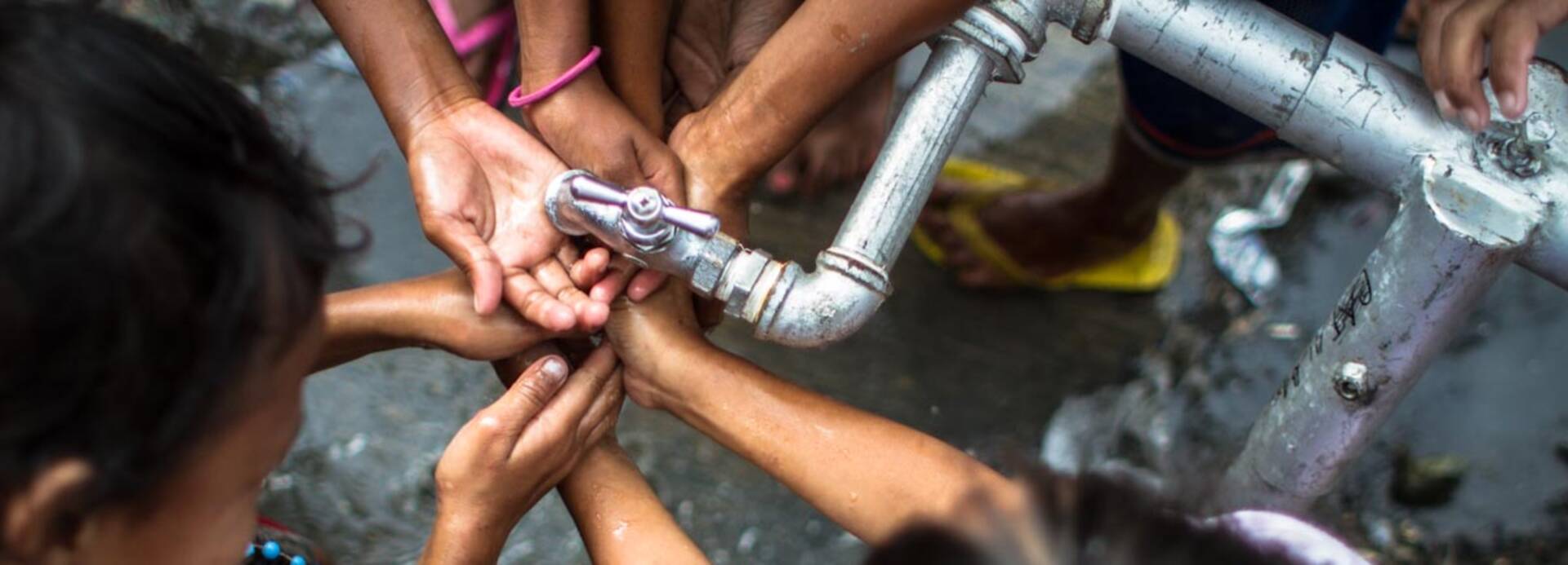 Kinder waschen sich die Hände unter einem Wasserhahn.