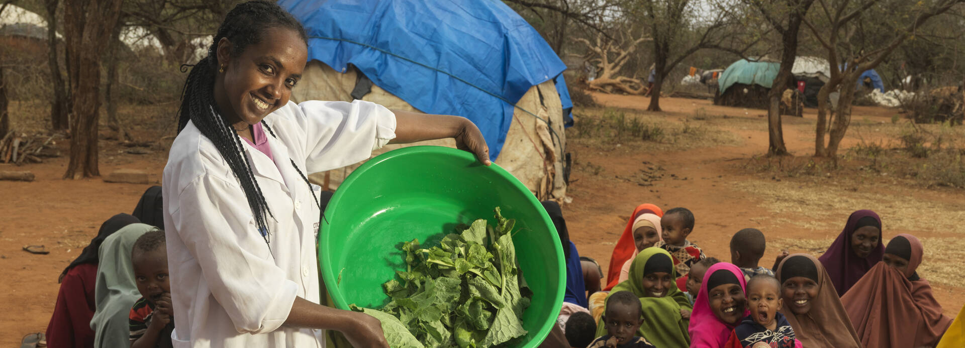 Gelaye Bekele ist Ernährungsspezialistin in Äthiopien und zeigt Familien das Kochen mit frischen Lebensmitteln; hier mit einer Schüssel Salat, im Hintergrund viele lachende Mütter mit Kindern