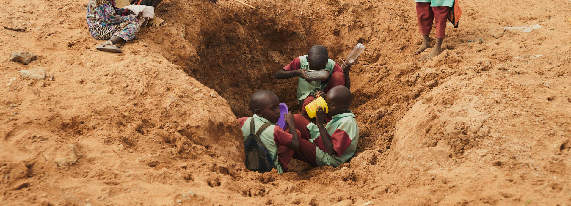 In Laresoro, Kenia, graben die Dorfbewohner Löcher, um Wasser zu finden. Hier halten Kinder auf dem Weg zur Schule an, um zu trinken und ihre Flaschen aufzufüllen, obwohl das Wasser verschmutzt und voller Bakterien ist. In Laresoro, Kenia, graben die Dorfbewohner Löcher, um Wasser zu finden. Hier halten Kinder auf dem Weg zur Schule an, um zu trinken und ihre Flaschen aufzufüllen, obwohl das Wasser verschmutzt und voller Bakterien ist.
