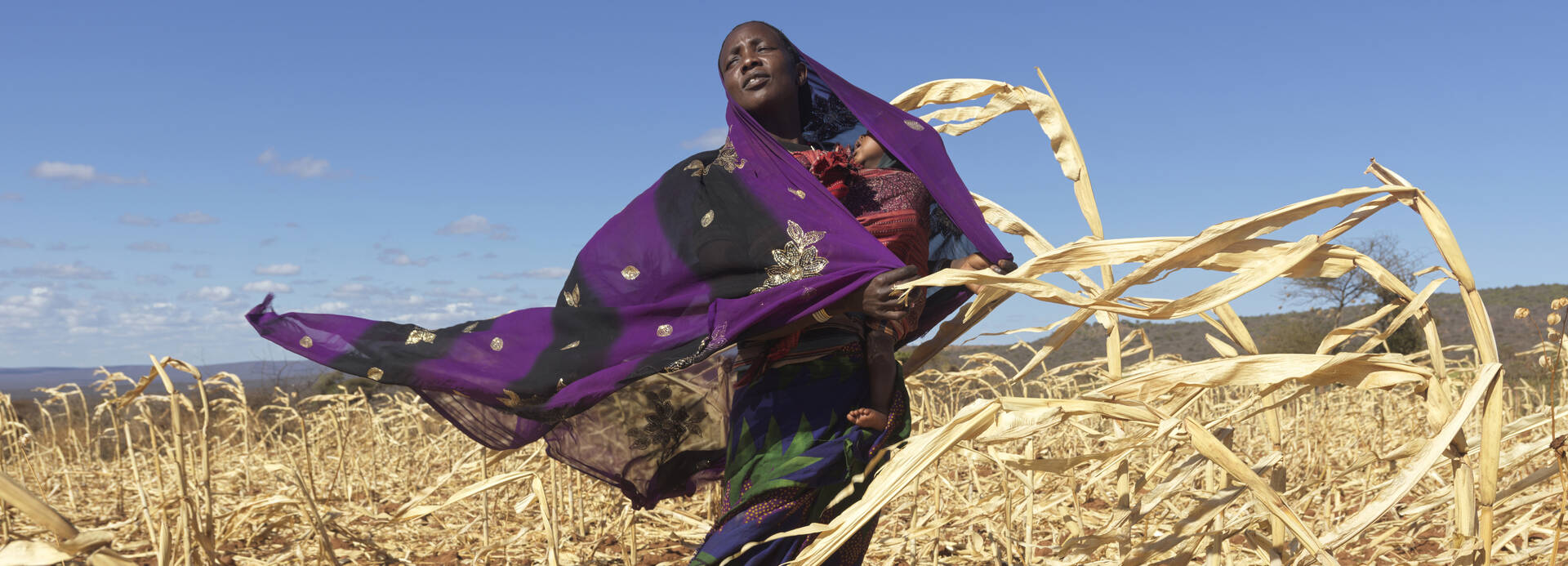 Loko aus Äthiopien steht mit ihrem Baby im Arm auf dem durch Dürre zerstörten Maisfeld.
