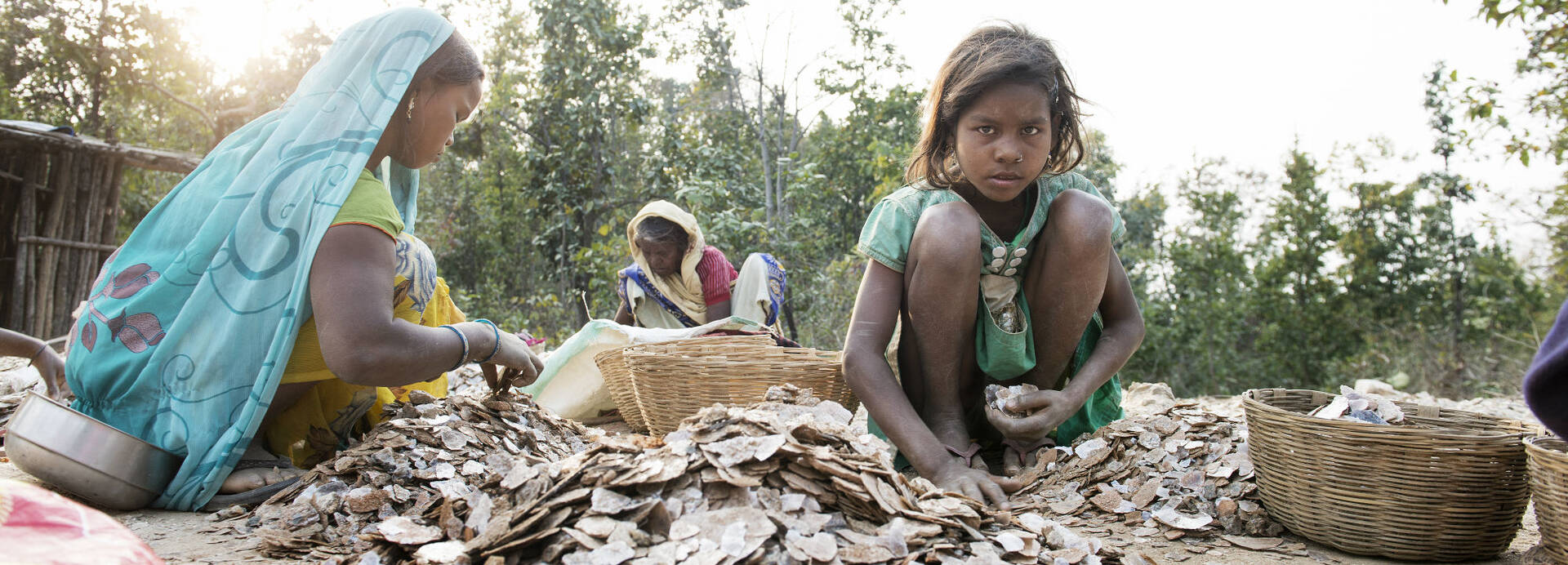 Kinderarbeit in Indien: Drei Kinder sitzen zwischen Steinen und Körben, um das Mineral Mica zu sortieren.