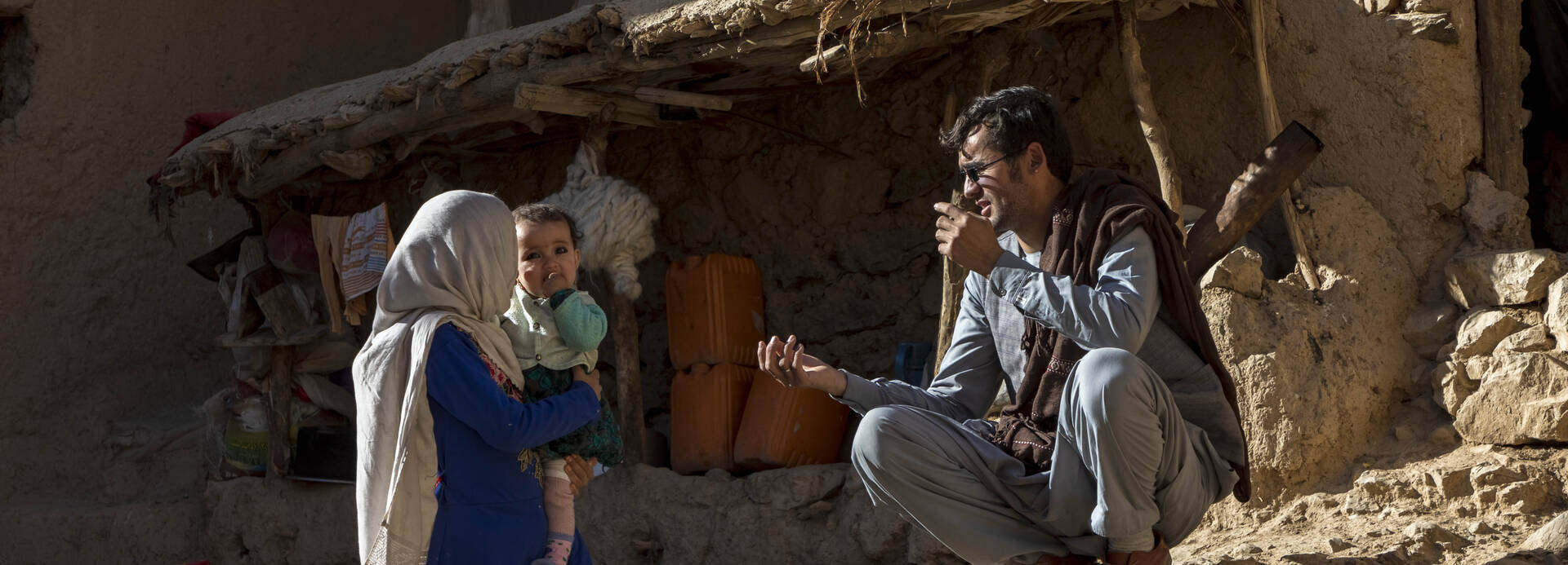 Eine dreiköpfige Familie vor ihrem halb zusammenfallenden Lehm-Haus in Afghanistan